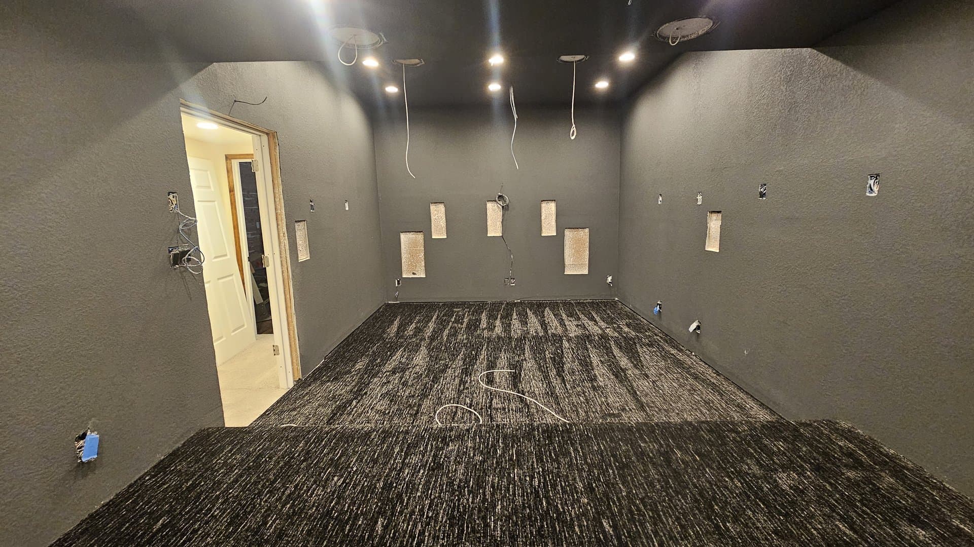 Bare cinema room before CineLuxe installation — painted walls, carpet, speaker cutouts